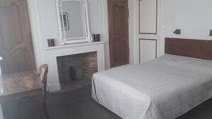 Une chambre à coucher avec un lit, une chaise en bois, une cheminée et un miroir.