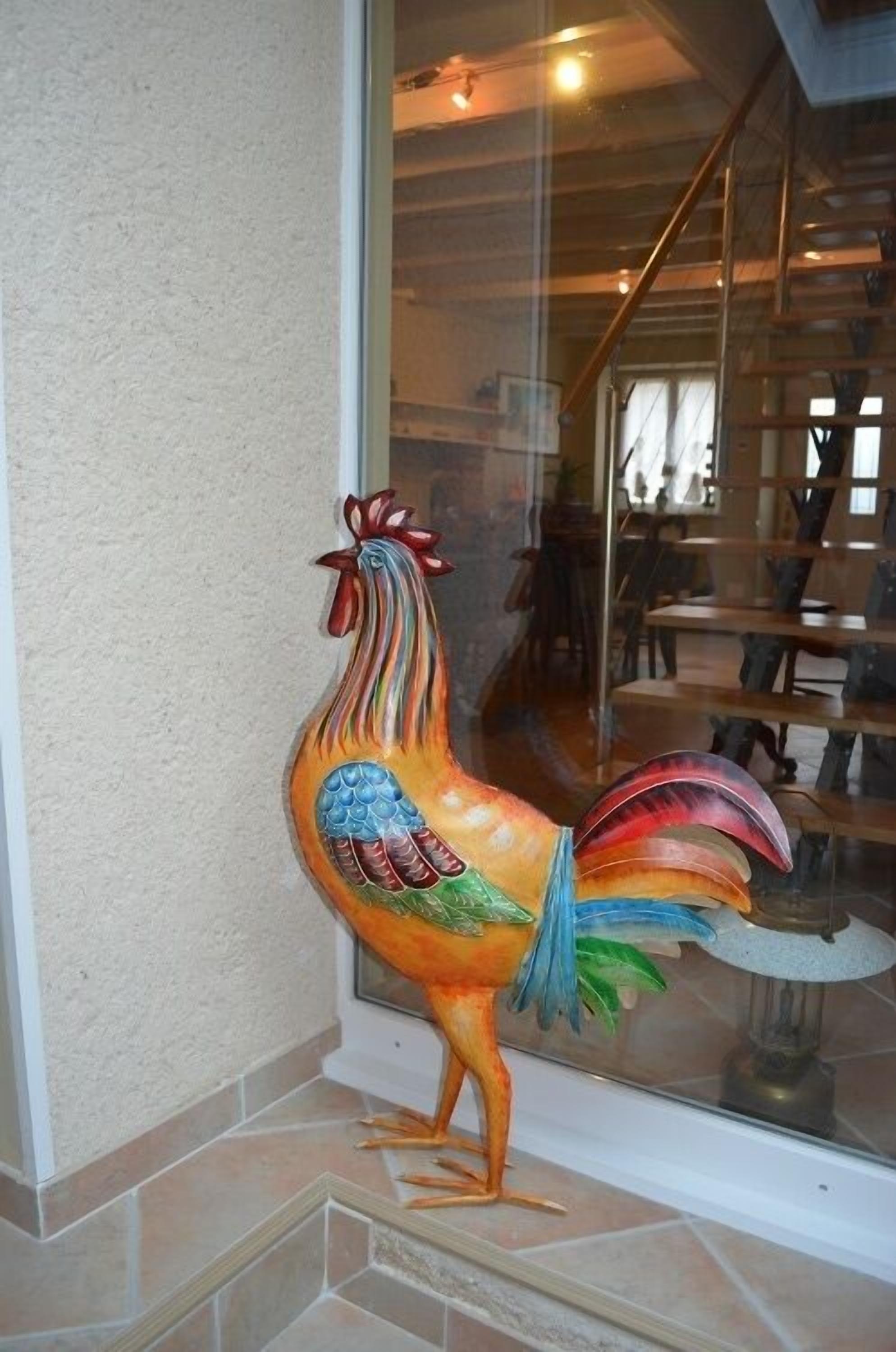 Eine bunte Hahnenstatue vor einem Gebäude mit Glastür.