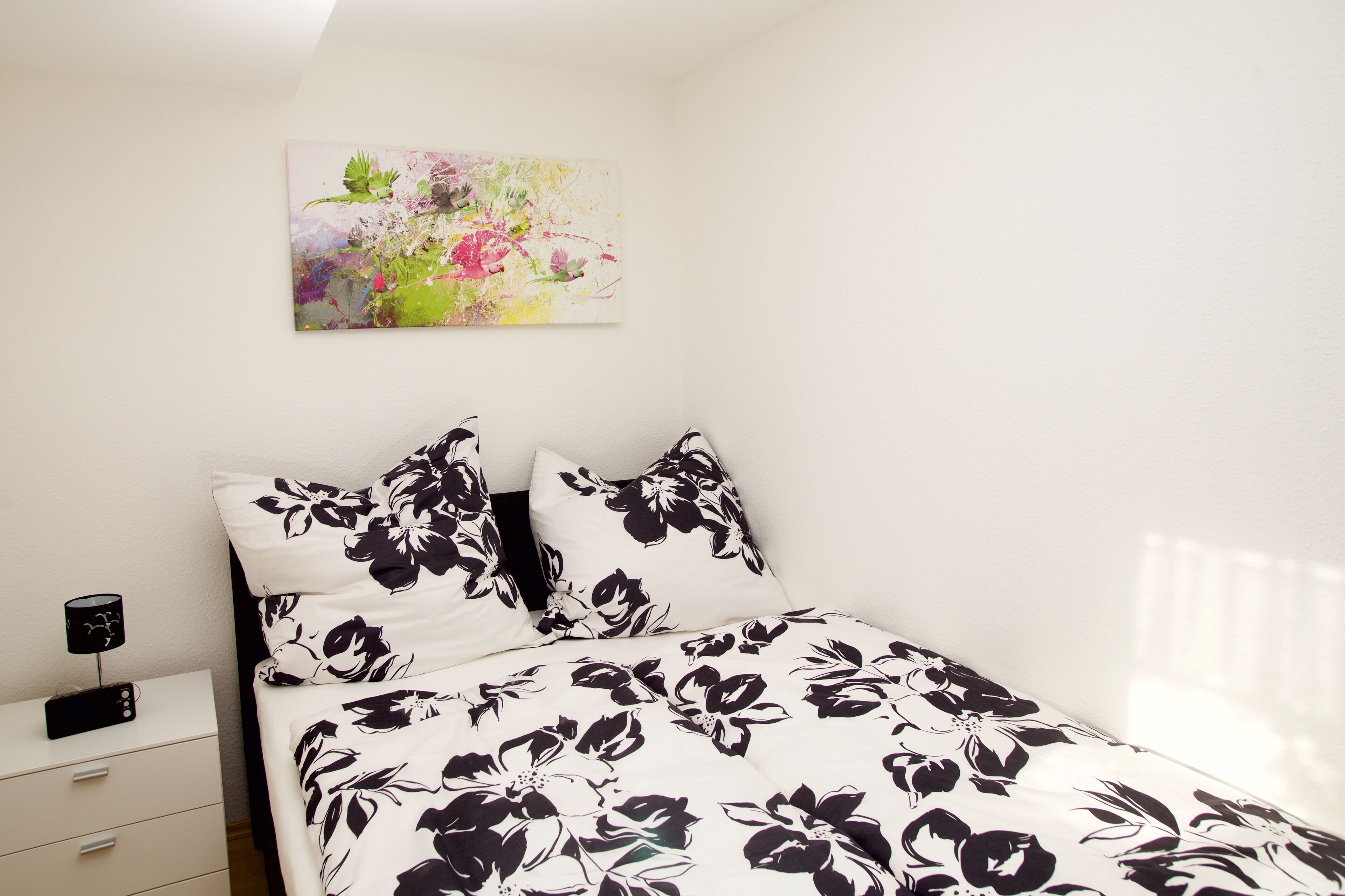 A bedroom with a bed, pillows, a nightstand, a lamp, and a painting on the wall.