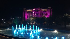 Nachtsicht auf ein Hotel mit einem Brunnen im Vordergrund und beleuchteter Beschilderung im Hintergrund.