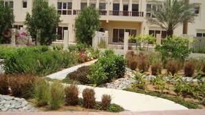 Ein angelegter Garten mit einem Pfad, verschiedenen Pflanzen und einem Gebäude mit Balkonen im Hintergrund.