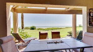 Eine überdachte Terrasse mit Tisch und Stühlen, mit Blick auf eine grüne Landschaft und das Meer.