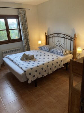 Un dormitorio con cama, dos lámparas de noche, una ventana con cortinas y un radiador.