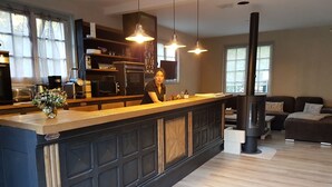 A modern kitchen with a central island, built-in appliances, pendant lighting, and a large window providing natural light. - House nest in the forest, near castel Compiègne, Pierrefonds and Chantilly (Saint-Jean-aux-Bois)