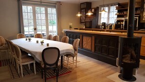 A dining area with a long table, chairs, and a central fireplace. - House nest in the forest, near castel Compiègne, Pierrefonds and Chantilly (Saint-Jean-aux-Bois)