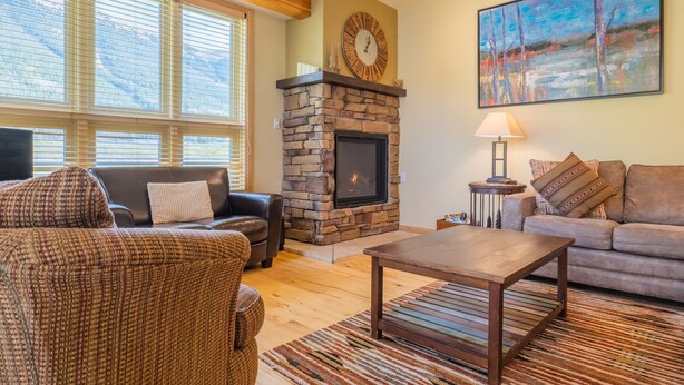 A cozy living room with a stone fireplace, a large clock, and a painting on the wall. - Private Home With A Beautiful Mountain Vista - Woods24 by RedAwning (Copper Mountain)