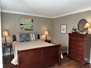 Une chambre à coucher avec un lit en bois, deux tables de chevet avec des lampes, une commode, un tableau encadré et une œuvre d’art murale.