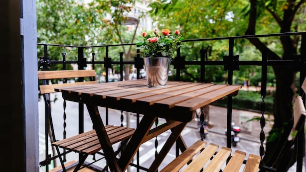 Ein Holztisch mit einem Metalltopf voller Blumen auf einem Balkon.