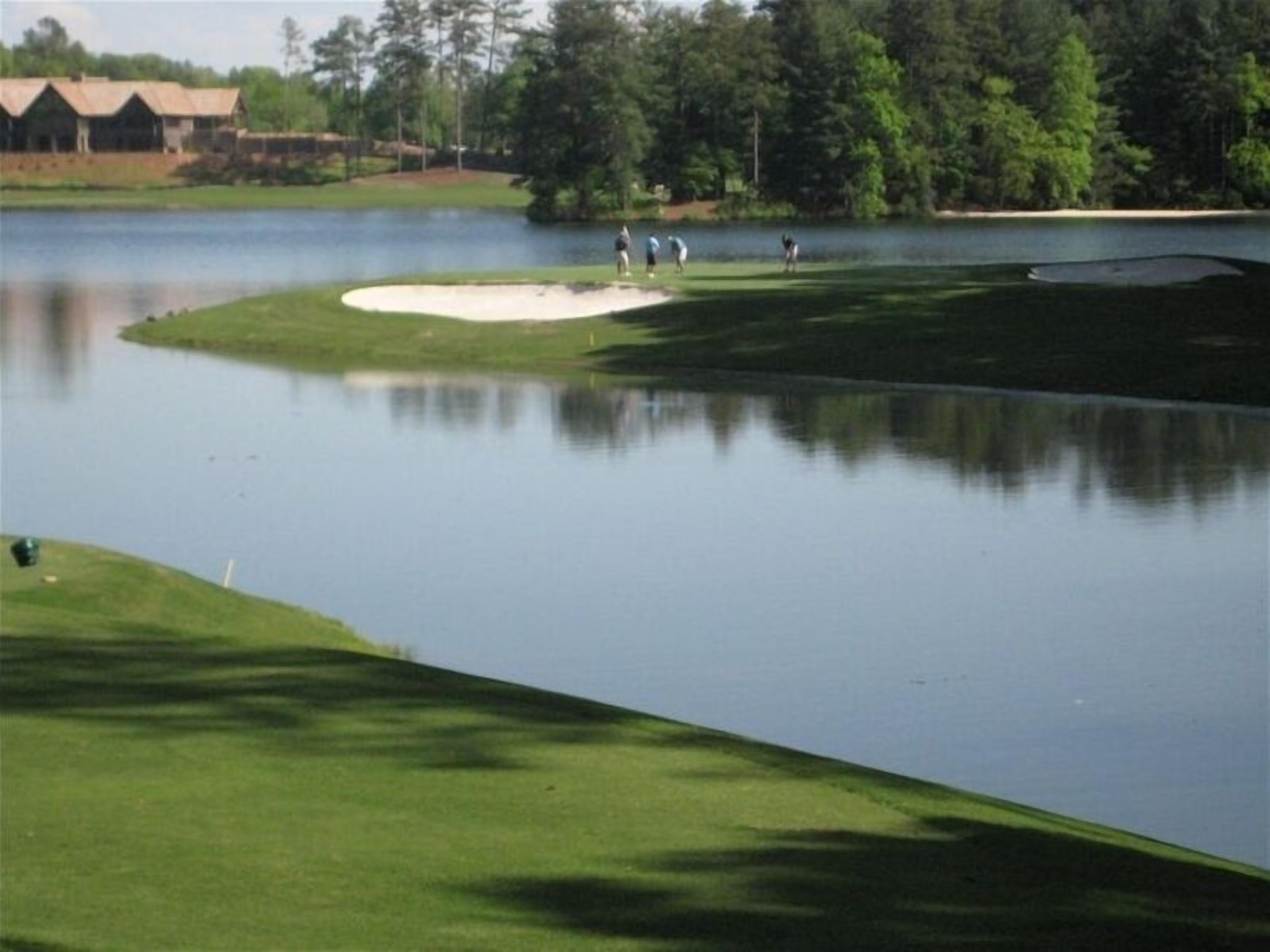 Un parcours de golf avec des obstacles d’eau, des bunkers de sable et un club-house en arrière-plan.
