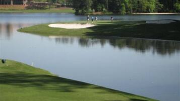 A golf course with a water hazard, sand bunkers, and a clubhouse in the background.