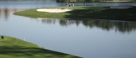 Un parcours de golf avec des obstacles d’eau, des bunkers de sable et un club-house en arrière-plan.