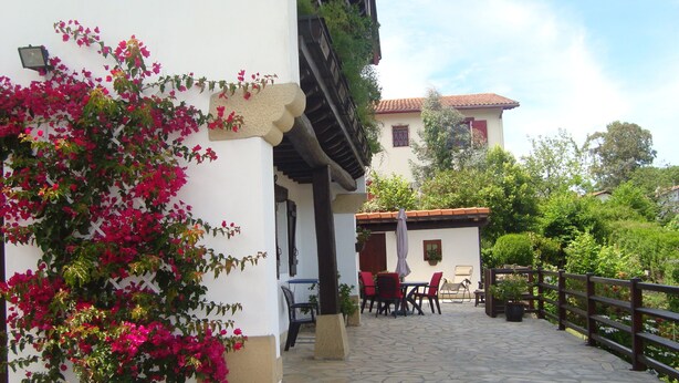 Un patio con suelo de piedra, mobiliario exterior y una pared blanca adornada con flores rosadas.