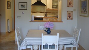 Un comedor con una mesa, sillas, un jarrón con flores y una cocina al fondo.