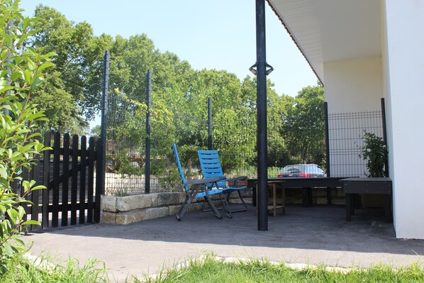 An outdoor patio area with a table and chairs, a fence, and trees in the background.
