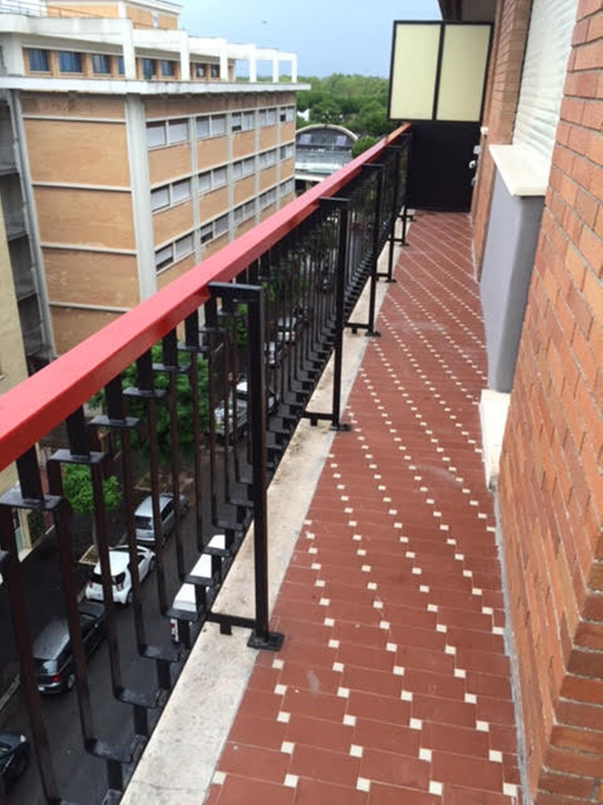 A red metal railing with a brick wall and a tiled walkway.
