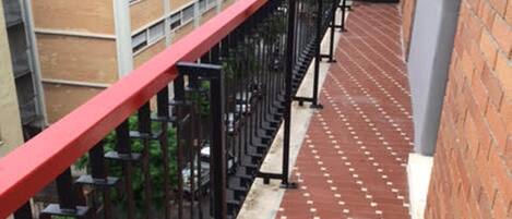 A red metal railing with a brick wall and a tiled walkway.