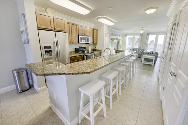 A modern kitchen with a granite countertop, stainless steel appliances, and white bar stools.