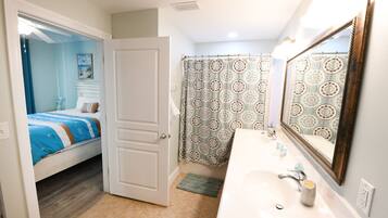 A bedroom with a bed, a bathroom with a sink and mirror, and a shower area.