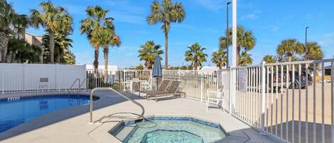 A pool area with a hot tub, lounge chairs, and palm trees.