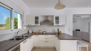 A modern kitchen with white cabinets, stainless steel appliances, and a large window. - Lovingly furnished house in a quiet location with heated pool and sea views (Gennadi, Rhodos)