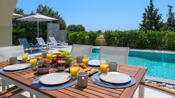 A breakfast table set with plates, glasses, and a fruit bowl, overlooking a pool and lounge chairs. - Lovingly furnished house in a quiet location with heated pool and sea views (Gennadi, Rhodos)