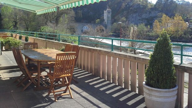 A terrace with wooden furniture and a view of a river and a tower. - Apt T3 air-conditioned, on the 1st floor of a character residence in CAHORS  (Cahors)