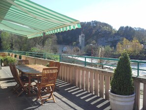 A terrace with wooden furniture and a view of a river and a tower.