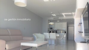 A modern living room with a sofa, chairs, and a coffee table. There is a kitchen area in the background with a dining table and chairs. - Exclusive apartment with frontal sea views (3 bedrooms / 2 bathrooms) (Arenales del Sol)
