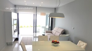 A modern dining area with a white table and chairs, a bowl of fruit, and a sofa in the background. - Exclusive apartment with frontal sea views (3 bedrooms / 2 bathrooms) (Arenales del Sol)