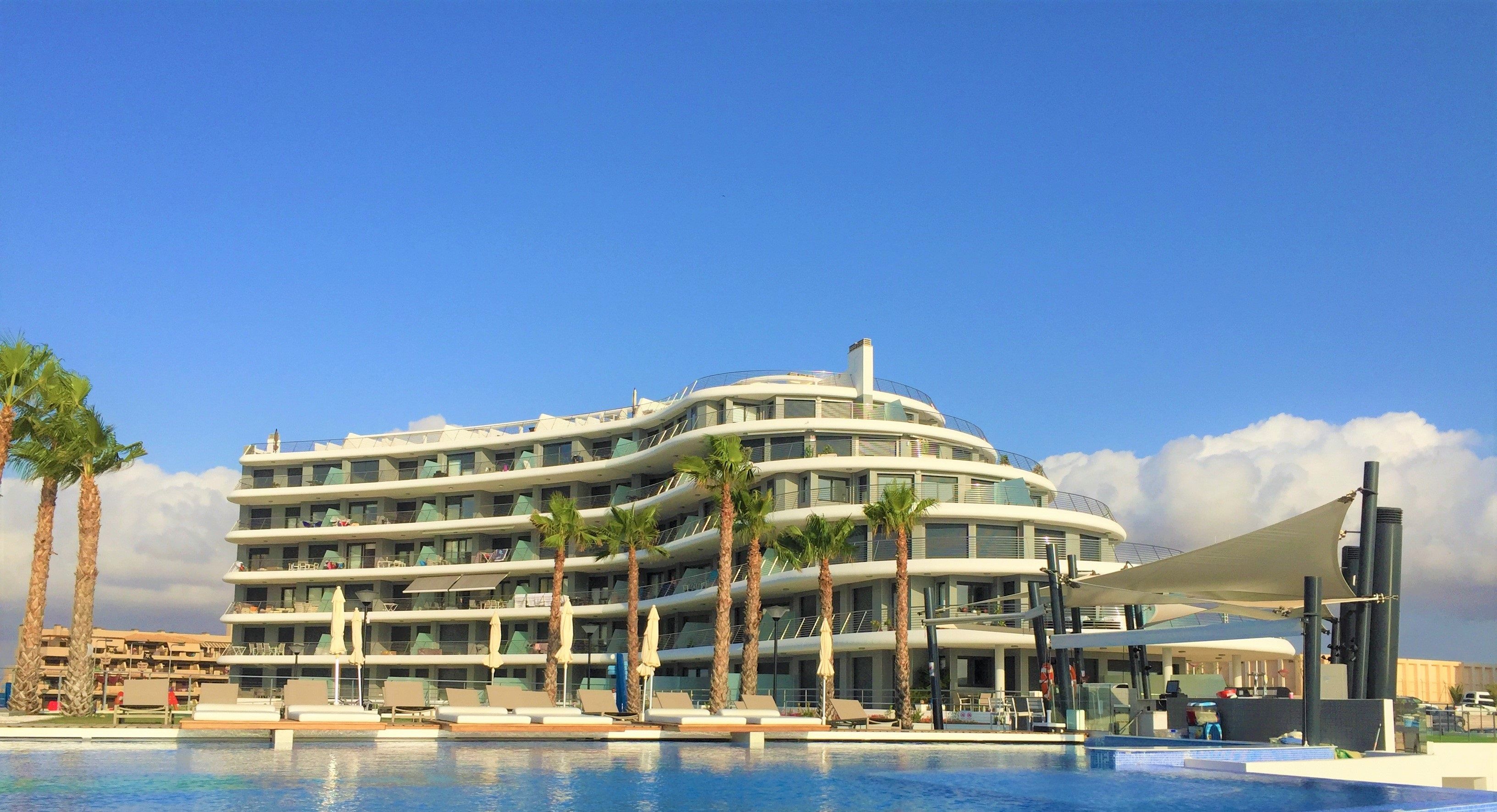 Un hôtel moderne doté d’une piscine, de palmiers et surplombant un ciel d’un bleu éclatant.