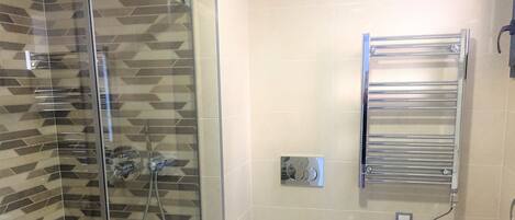A modern bathroom with a glass shower enclosure, a white toilet, and a chrome towel rack.