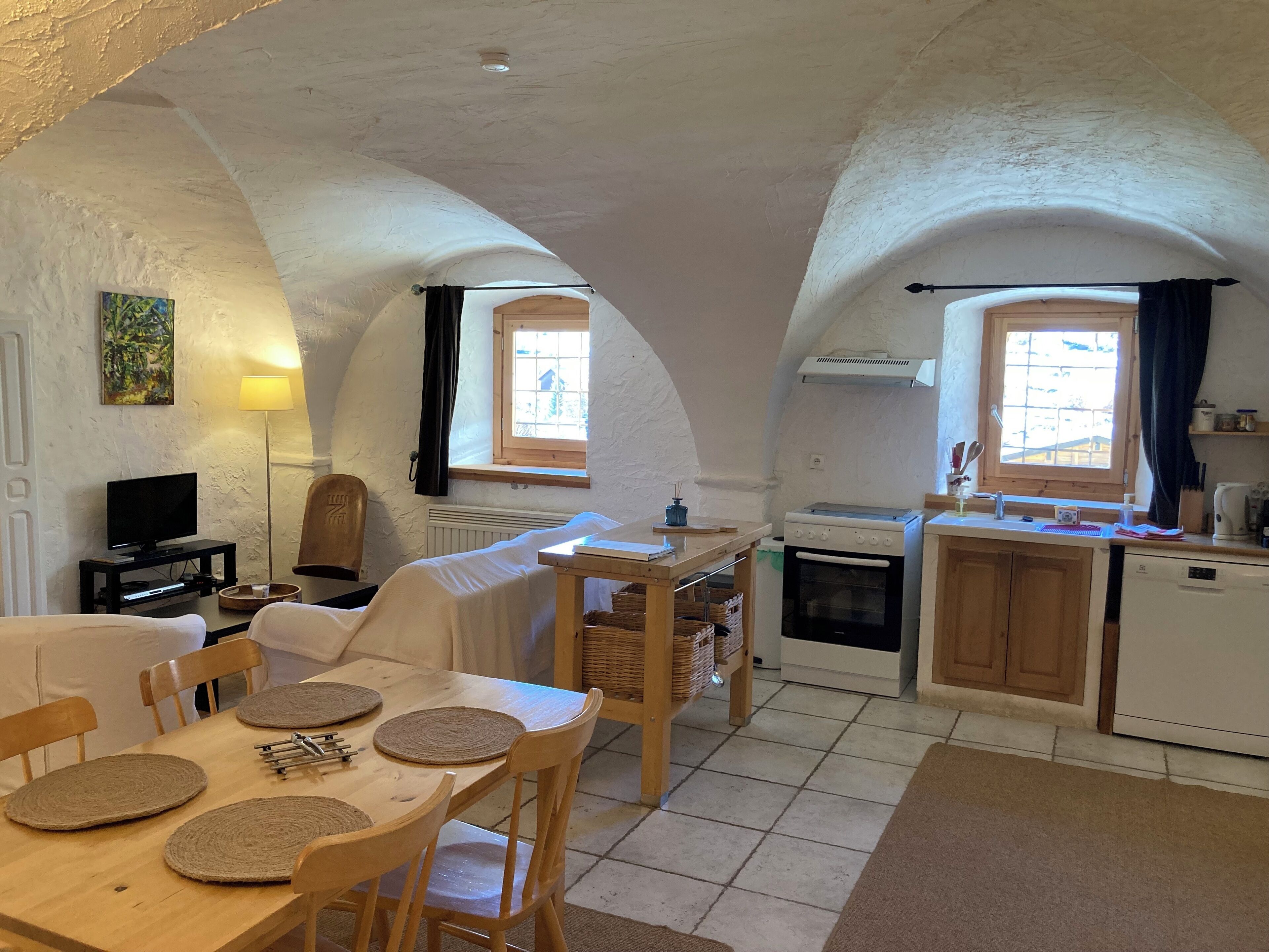 A cozy kitchen with a dining area, white walls, wooden cabinets, and a tiled floor.