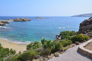A coastal landscape with rocky terrain, a sandy beach, and clear blue sea.