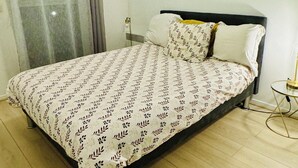 Una cama bien hecha con una colcha estampada, una mesita de noche con lámpara y una ventana con cortinas.
