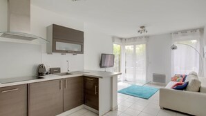 Una cocina moderna con horno empotrado, microondas y cafetera. Hay una zona de comedor con sofá y televisor.