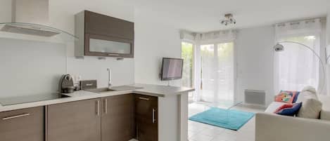 A modern kitchen with a built-in oven, a microwave, and a coffee maker. There is a dining area with a sofa and a TV.