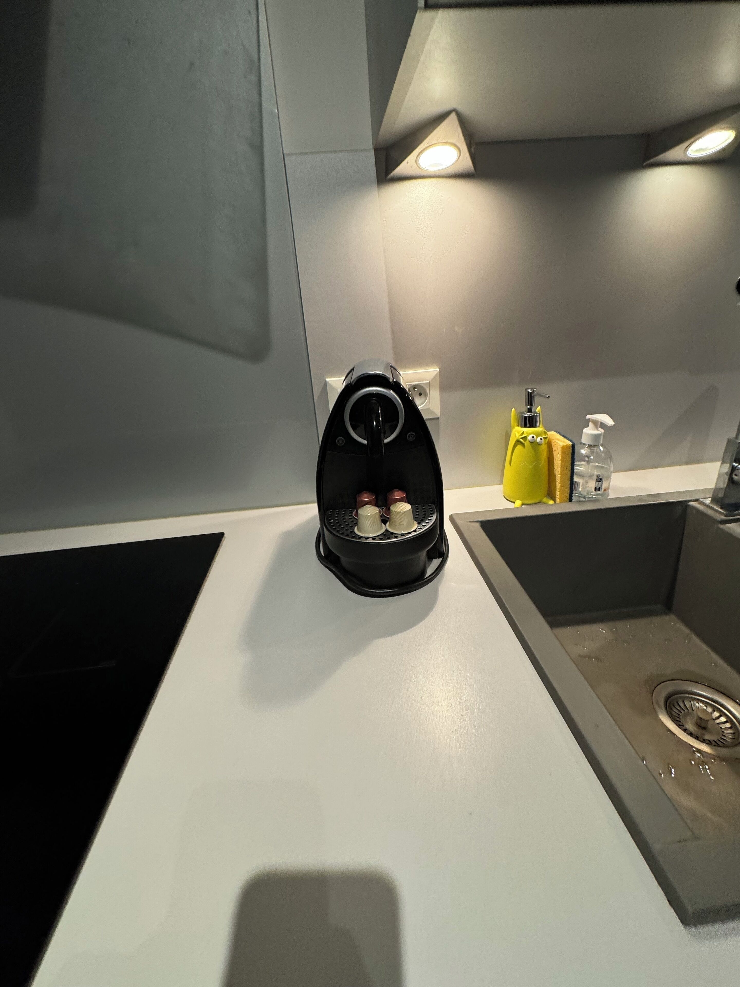 A kitchen with a black air fryer, a yellow sponge, and a bottle of hand soap on the counter.