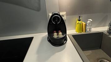 Een keuken met een zwarte heteluchtfriteuse, een gele spons en een fles handzeep op het aanrecht.