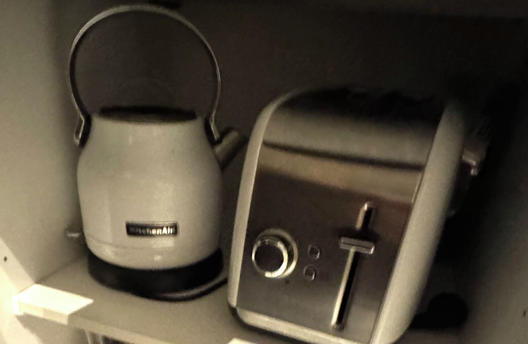 A kettle and a toaster on a shelf.