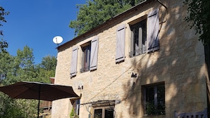 A rustic stone building with a wooden door, a satellite dish, and a small outdoor seating area with a table and chairs.