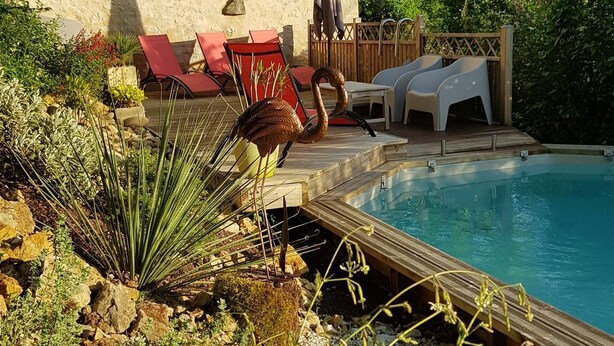 A pool area with a stone building, lounge chairs, and a wooden deck.