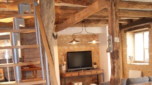 A rustic interior with a wooden staircase, a flat-screen TV, and a dining area.