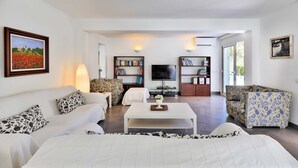 Ein modernes Wohnzimmer mit einer Couch, Sesseln, einem Couchtisch und zwei Bücherregalen voll mit Büchern und einem Flachbildfernseher.