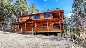 Une cabane en bois à deux étages, dotée d’une véranda et entourée d’arbres.