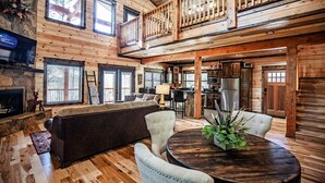 Un intérieur spacieux de chalet en bois, comprenant un salon, un coin repas, une cuisine et un balcon.