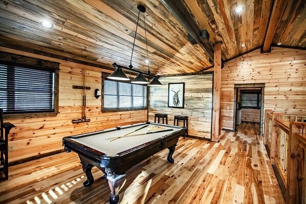 Un intérieur en bois avec une table de billard, des luminaires suspendus et un tableau encadré au mur.