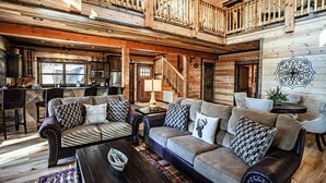Un vaste espace de vie doté d’un haut plafond, de poutres en bois, d’un escalier et d’un coin cuisine.