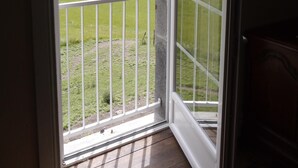 A room with a sliding glass door leading to a balcony with a view of a green landscape and trees.