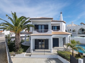 A two-story house with a tiled roof, a balcony, and a swimming pool.