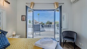 Une chambre avec un lit, une chaise, un balcon avec vue et une porte.